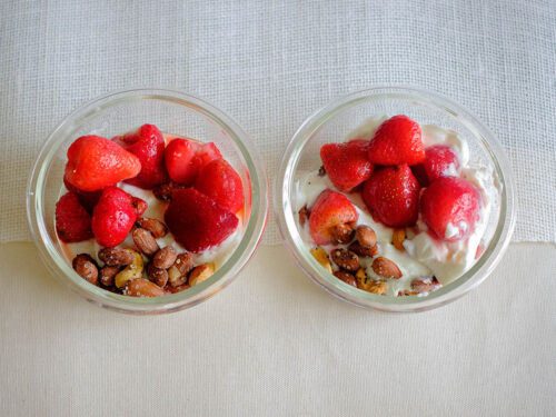 round glass containers with yogurt topped with strawberries and mixed nuts