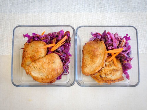 square glass meal prep containers with pork chops and sauteed red cabbage