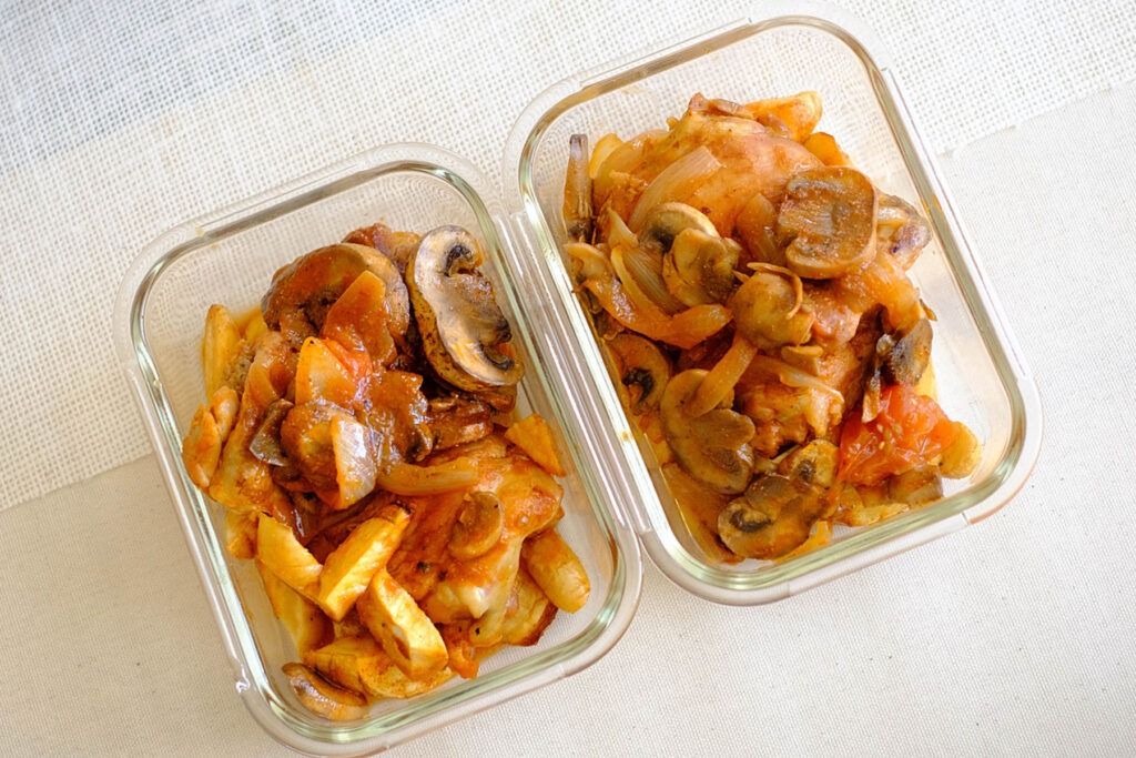 glass meal prep containers with one pot chicken in tomato sauce with sliced mushrooms and parsnips