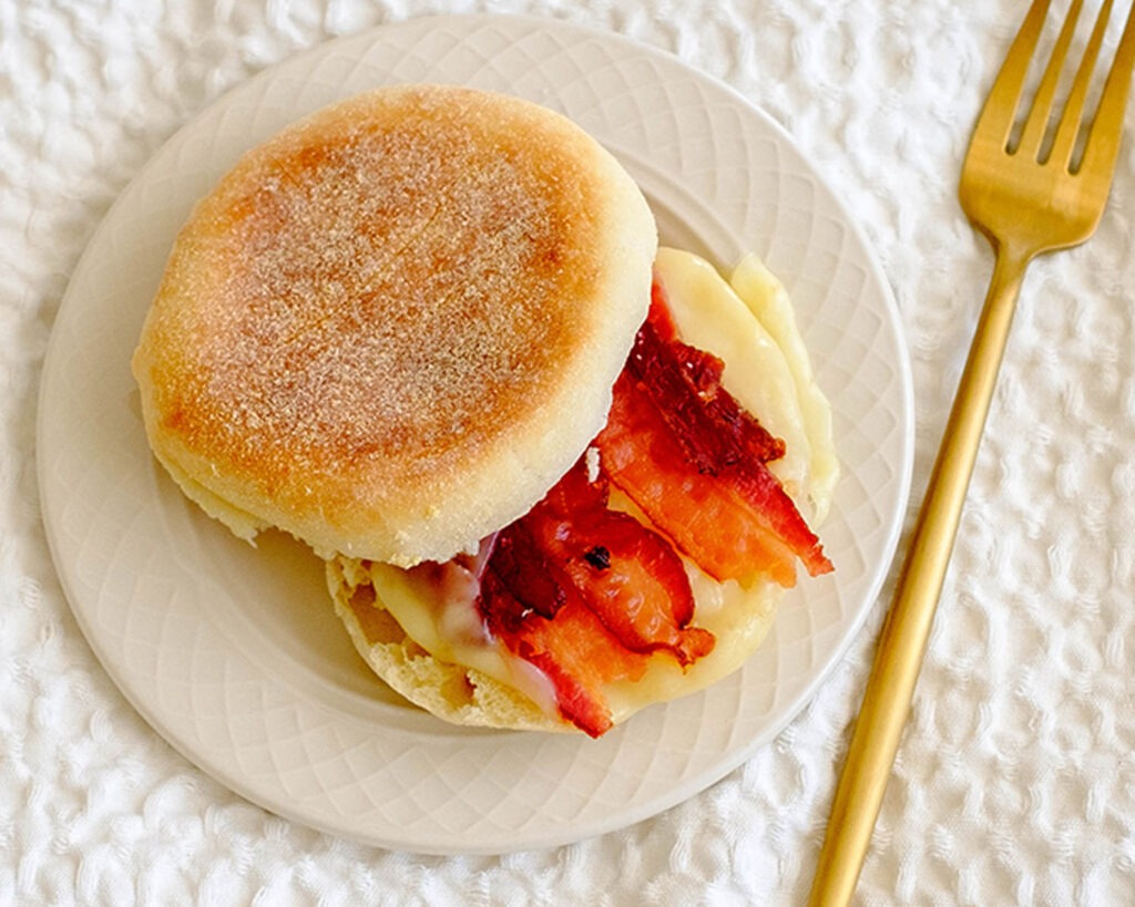 round plate with english muffins, bacon slices, and sliced cheese for a breakfast meal prep