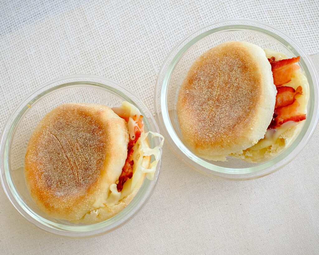 english muffins, bacon slices, and sliced cheese in containers for breakfast meal prep