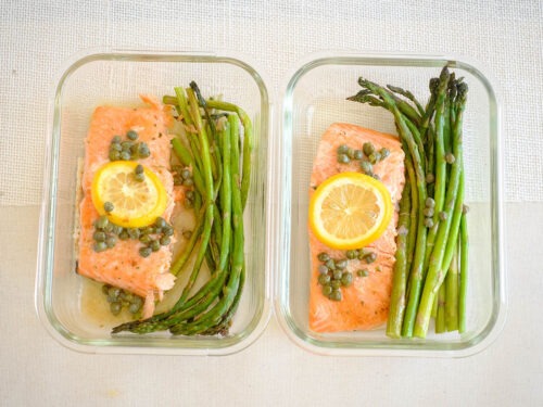 glass rectangle meal prep containers with salmon fillet topped with lemon, capers, and asparagus