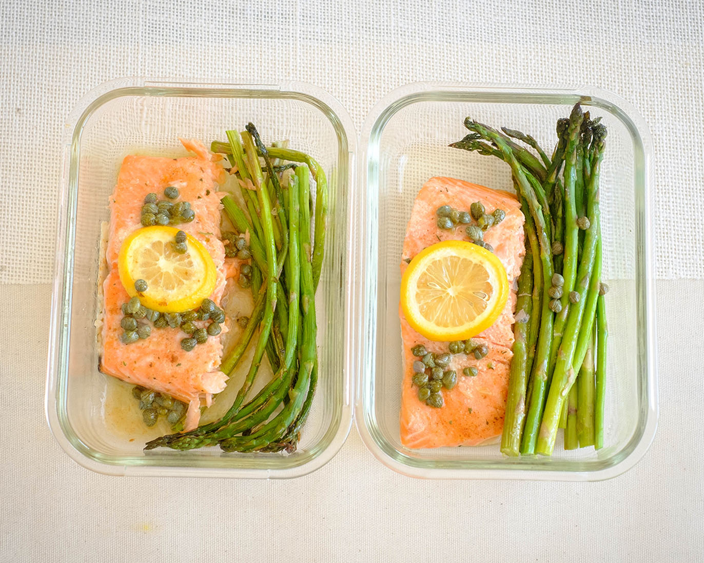 glass rectangle meal prep containers with salmon fillet topped with lemon, capers, and asparagus