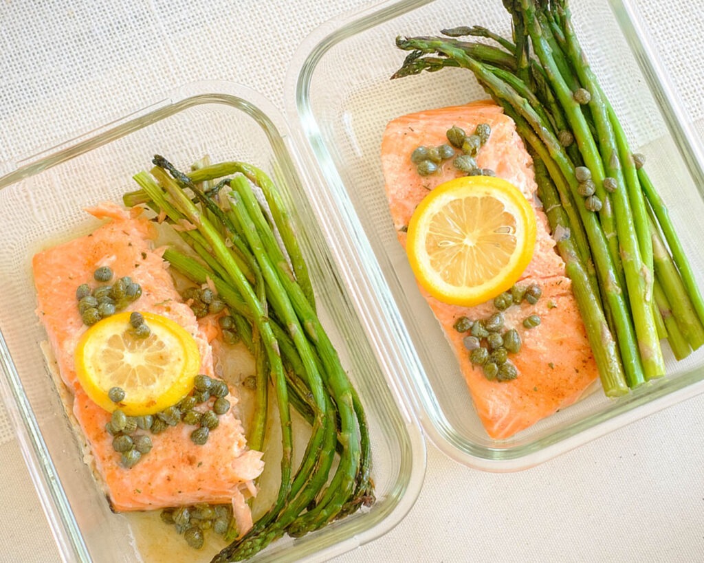 rectangle glass meal prep containers with salmon fillet topped with lemon, capers, and asparagus