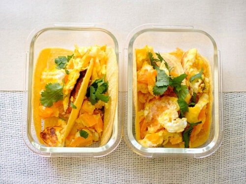 glass rectangular meal prep containers with corn tortillas topped with scrambled eggs and chopped cilantro and bell pepper