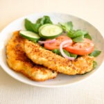 crispy panko breaded chicken tender with salad, sliced cucumbers, tomatoes, and red onions