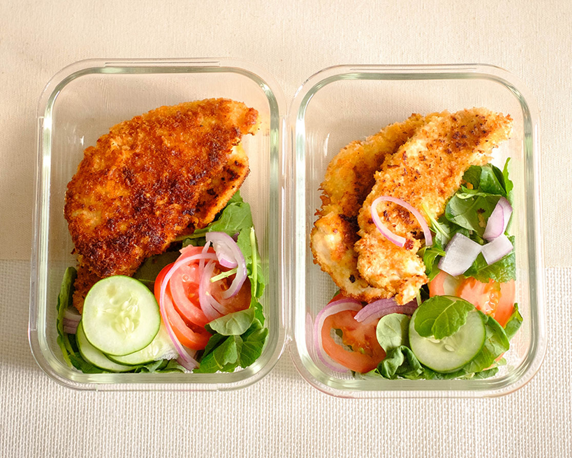 crispy panko breaded chicken tender with salad, sliced cucumbers, tomatoes, and red onions