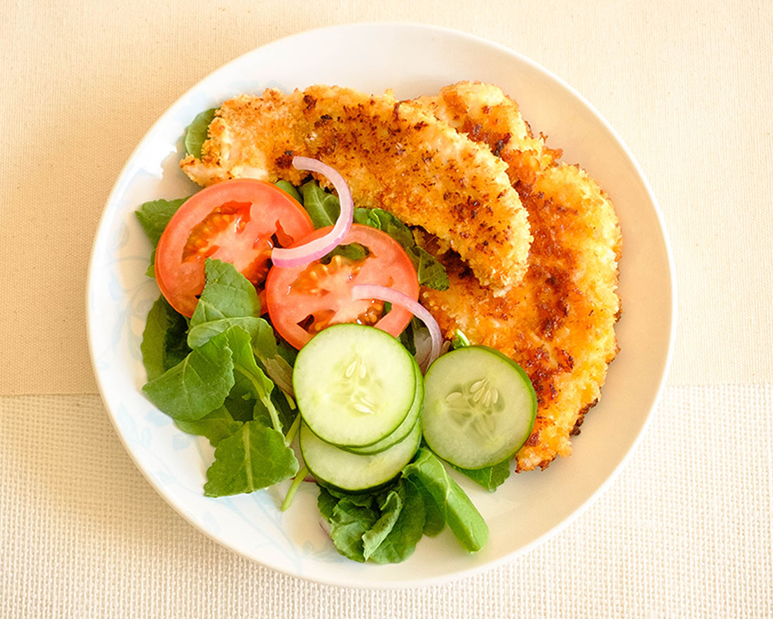 crispy panko breaded chicken tender with salad, sliced cucumbers, tomatoes, and red onions