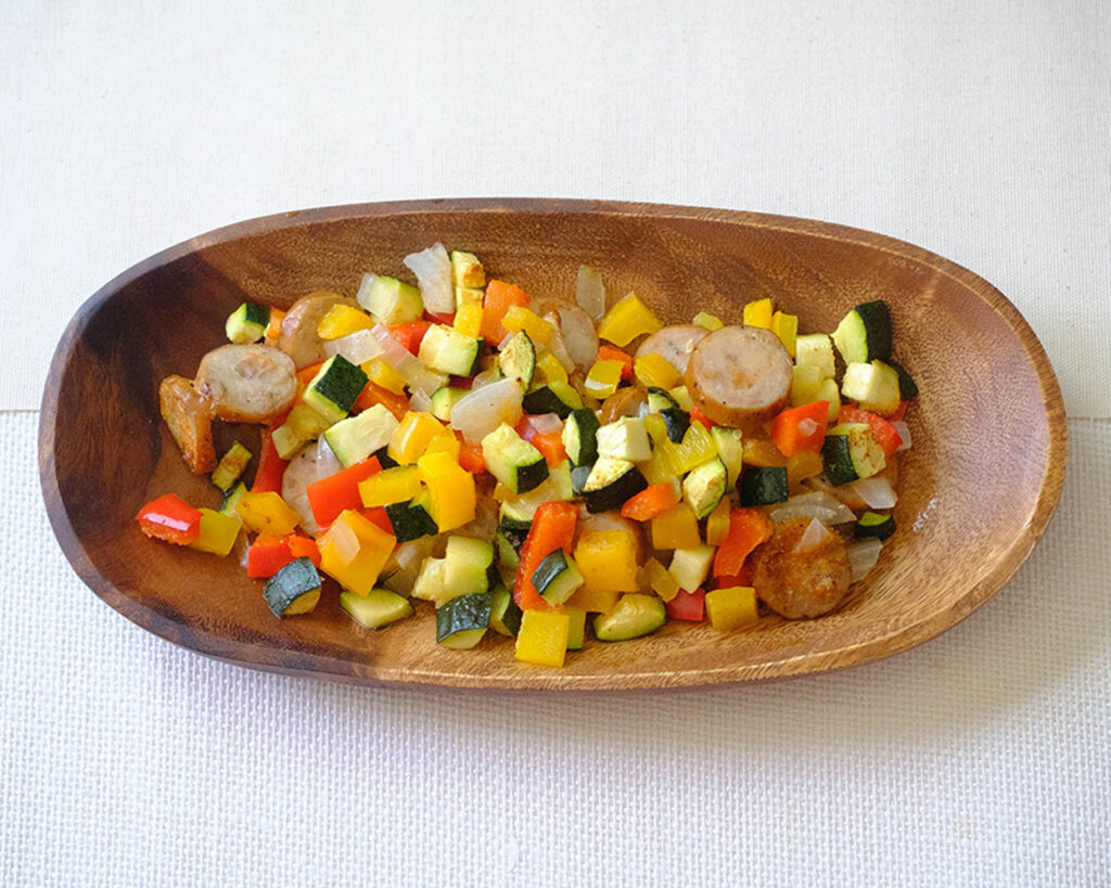 round wooden plate with a healthy lunch of sliced sausage and diced zucchini, bell peppers, and red onions