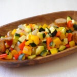 round wooden plate with sliced sausage and diced zucchini, bell peppers, and red onions