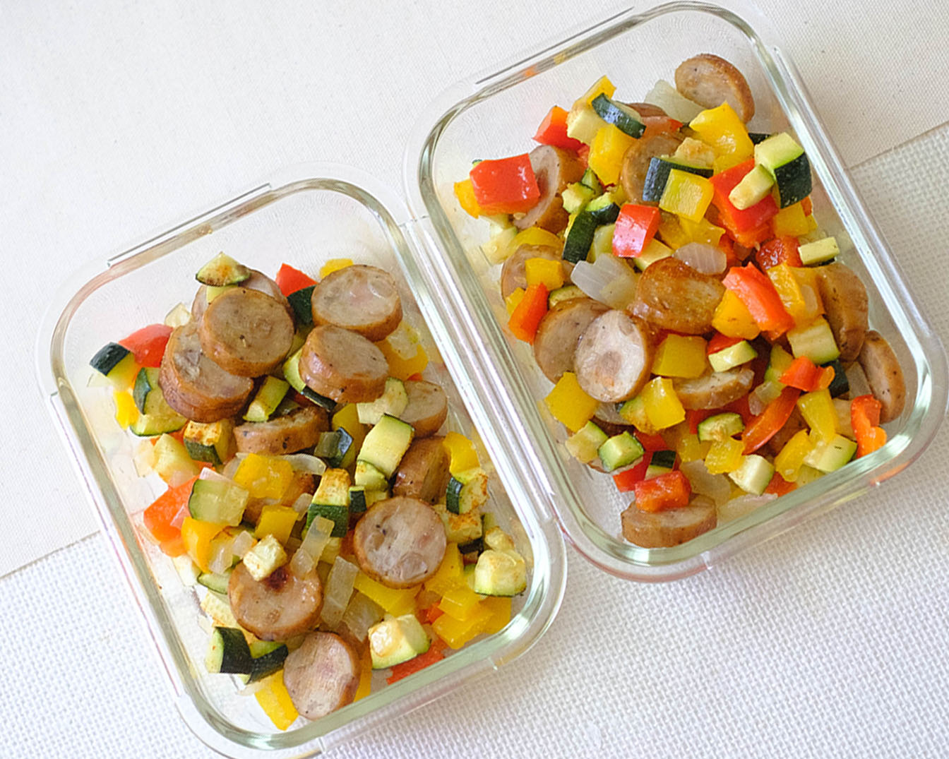 rectangular glass meal prep containers with a healthy lunch of sliced sausage and diced zucchini, bell peppers, and red onions