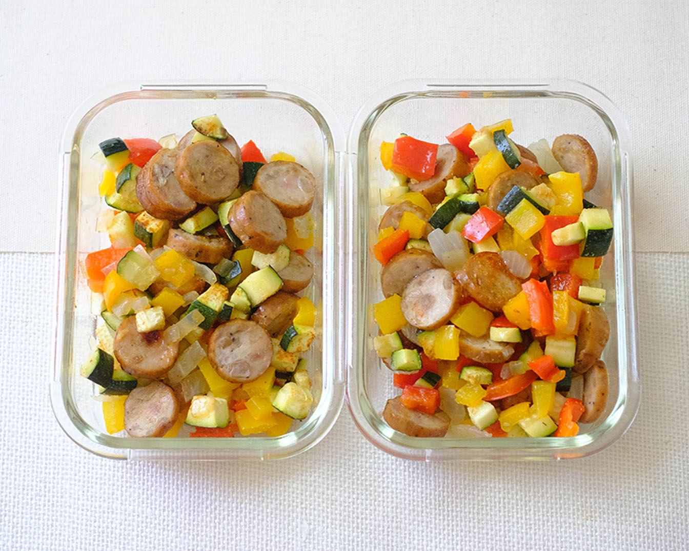 rectangular glass meal prep containers with sliced sausage and diced zucchini, bell peppers, and red onions